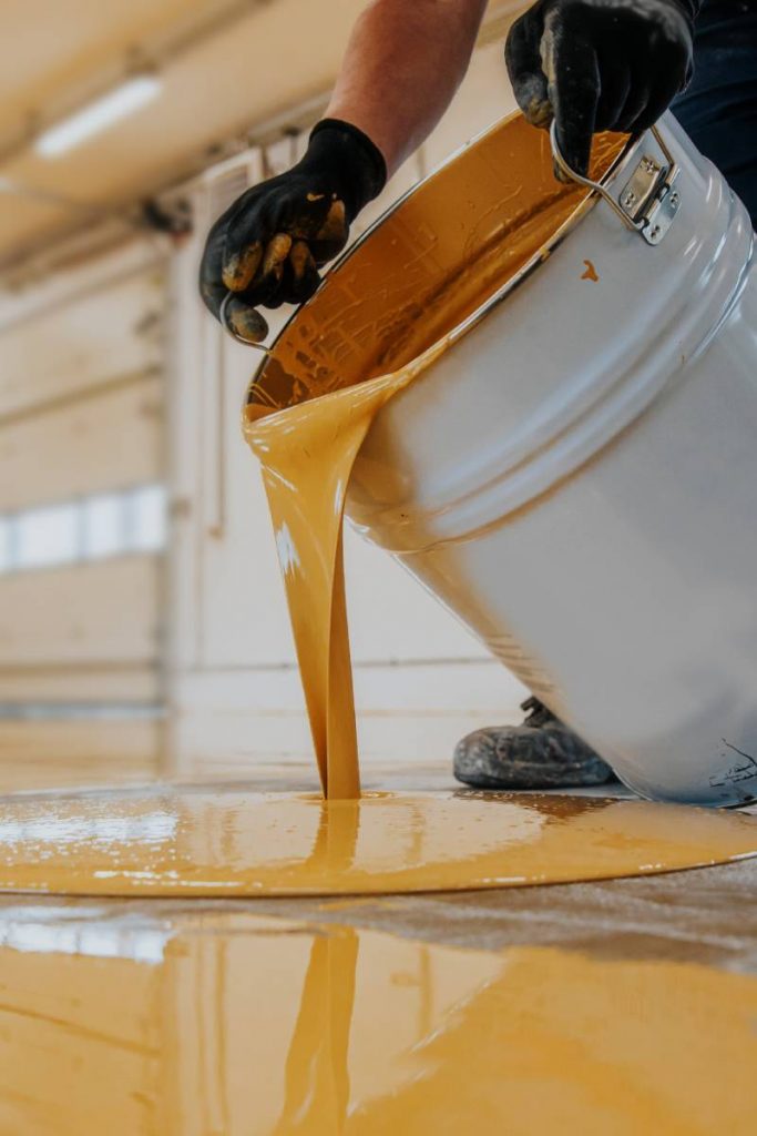 Worker applying a yellow epoxy resin bucket on floor.