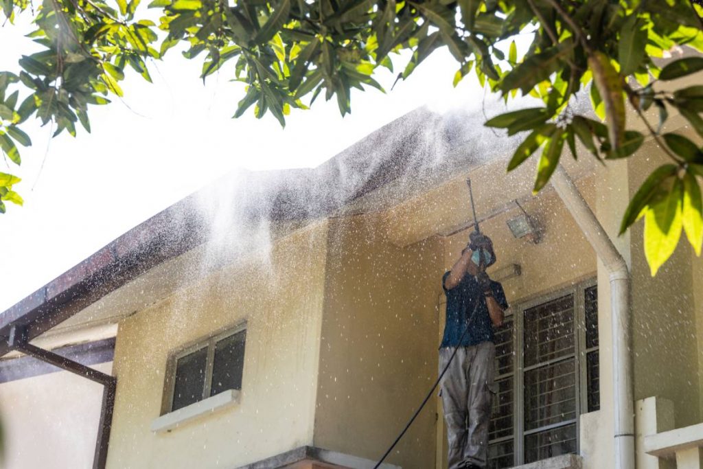 Worker using high pressure water jet spray gun to wash and clean dirt from roof ceiling at residential building